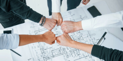Close up view of hands of business people that celebrating success in the office above building plan that is on table.