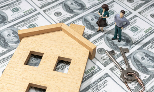 Investing in a house concept. Real estate prices. Toy house and figurine couple on dollar banknote background